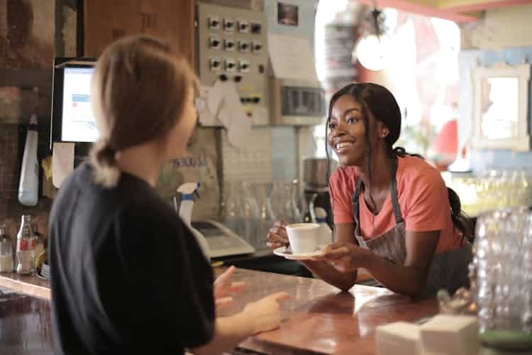 Female barista giving a coffee in a white cup to a customer