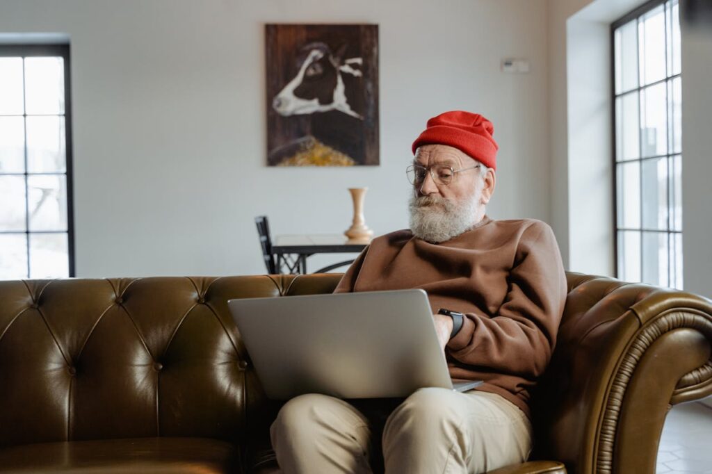 Man in sweater and beanie using laptop on leather couch